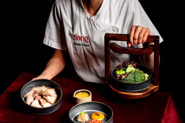a chef sitting behind a table with a red table cloth with various asian dishes in front of them