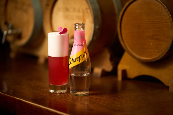 a cocktail with a schwepps bottle beside it infront of wodden barrels