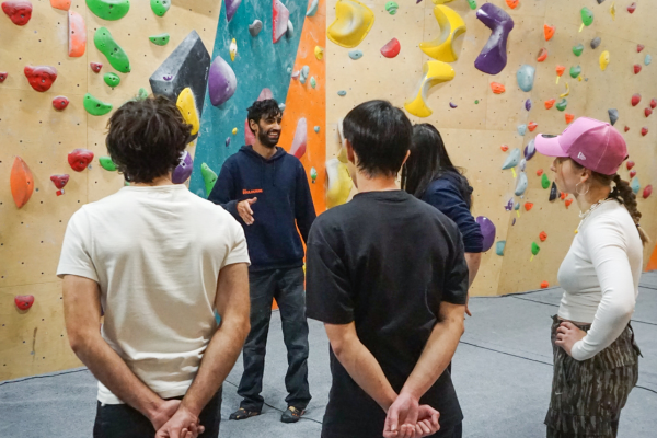 three people in a bouldering space, listenting to another person who is standing in front of them and talking